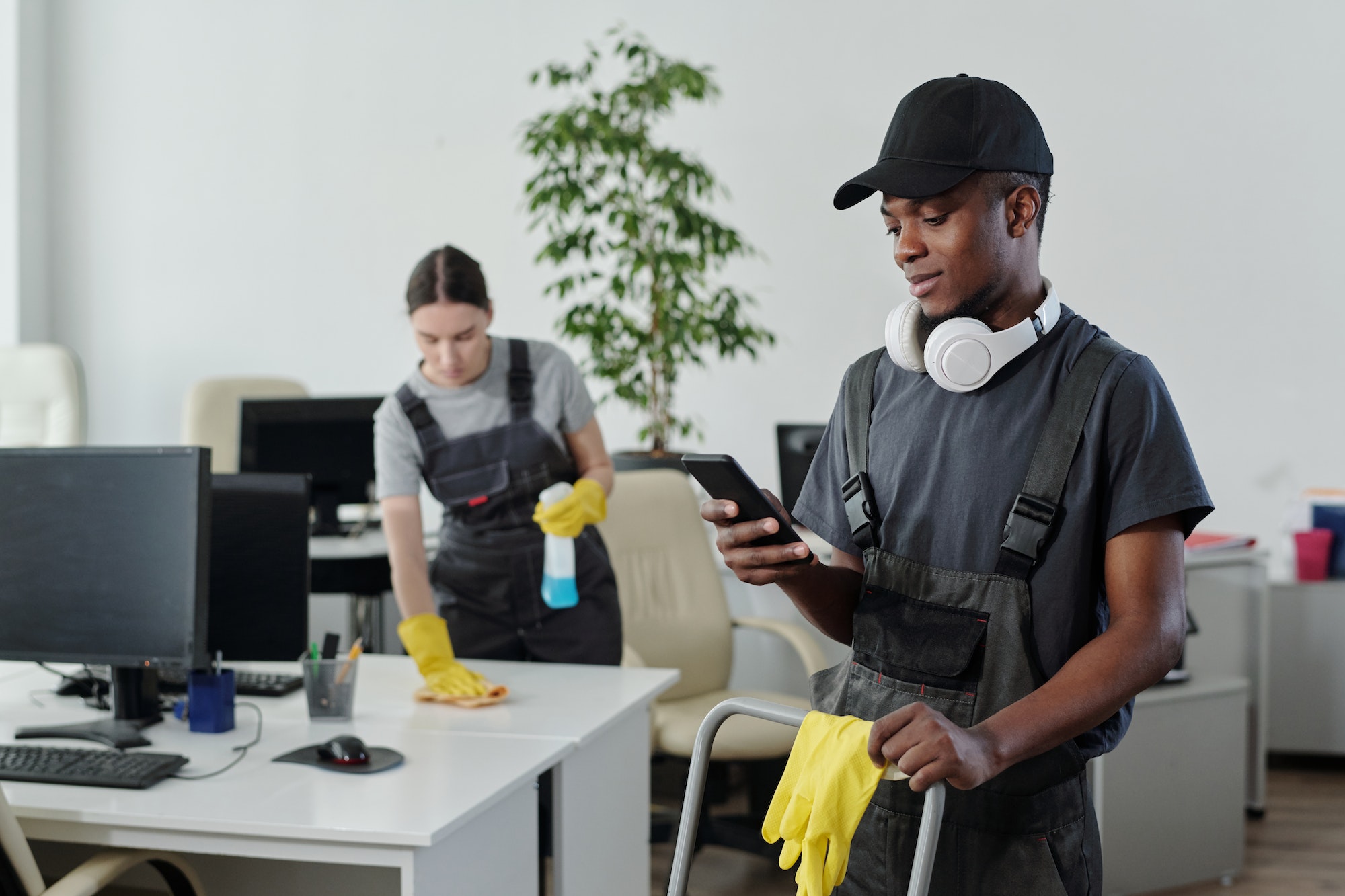 Young male cleaner in workwear choosing music in playlist during work in office